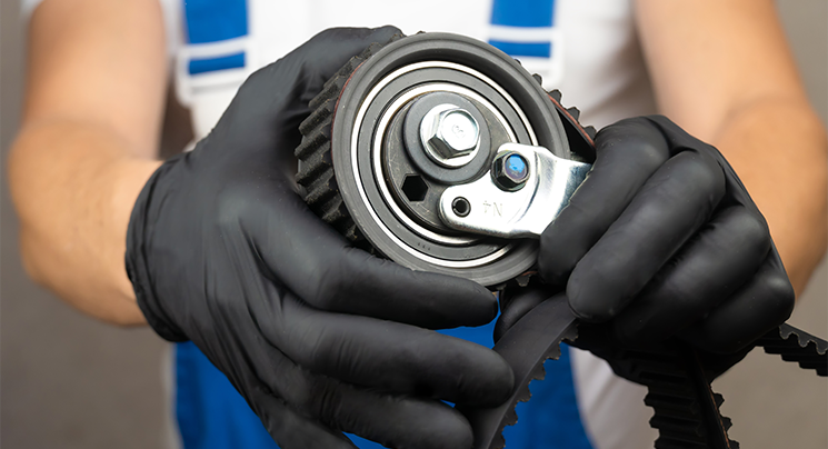 Black nitrile gloves holding a timing belt tensioner